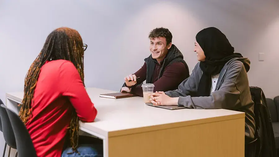 Three students sitting at a table having conversation.