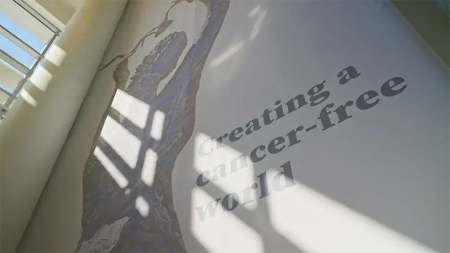 A wall mural of an abstract human figure with sunlight casting shadows across it, next to the words “Creating a cancer‑free world.”