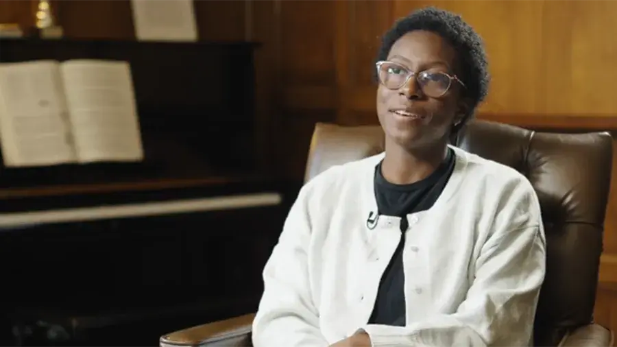 Individual sitting in a chair in front of a piano being interviewed.