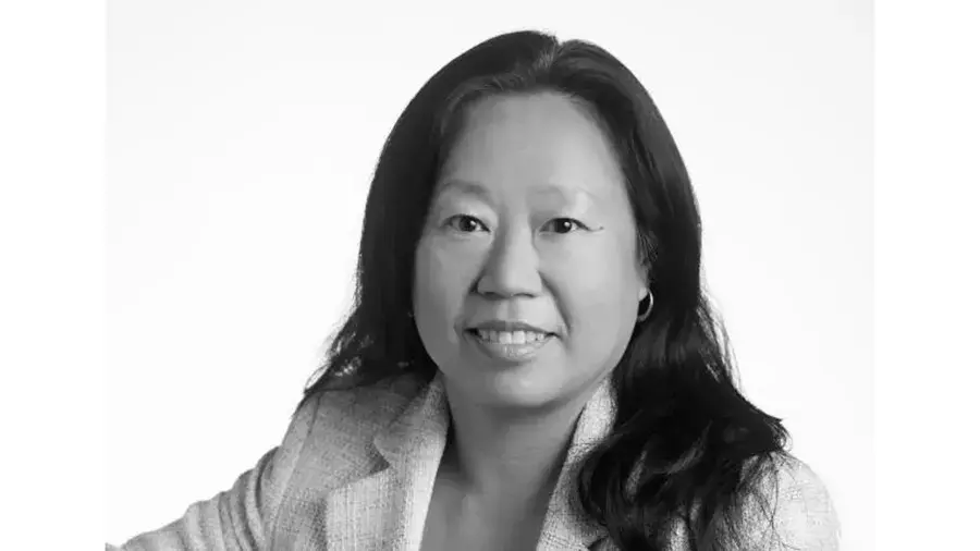 A person with long hair is shown in a portrait-style image, wearing a textured blazer against a plain background.