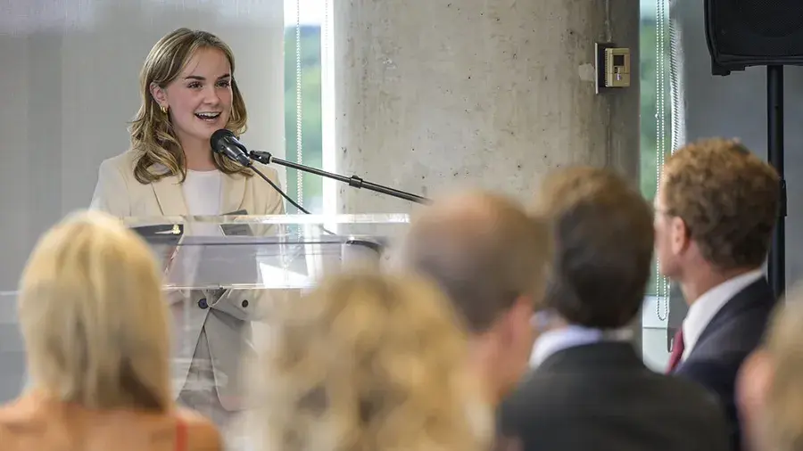 Ally standing behind a podium speaking to a crowd.