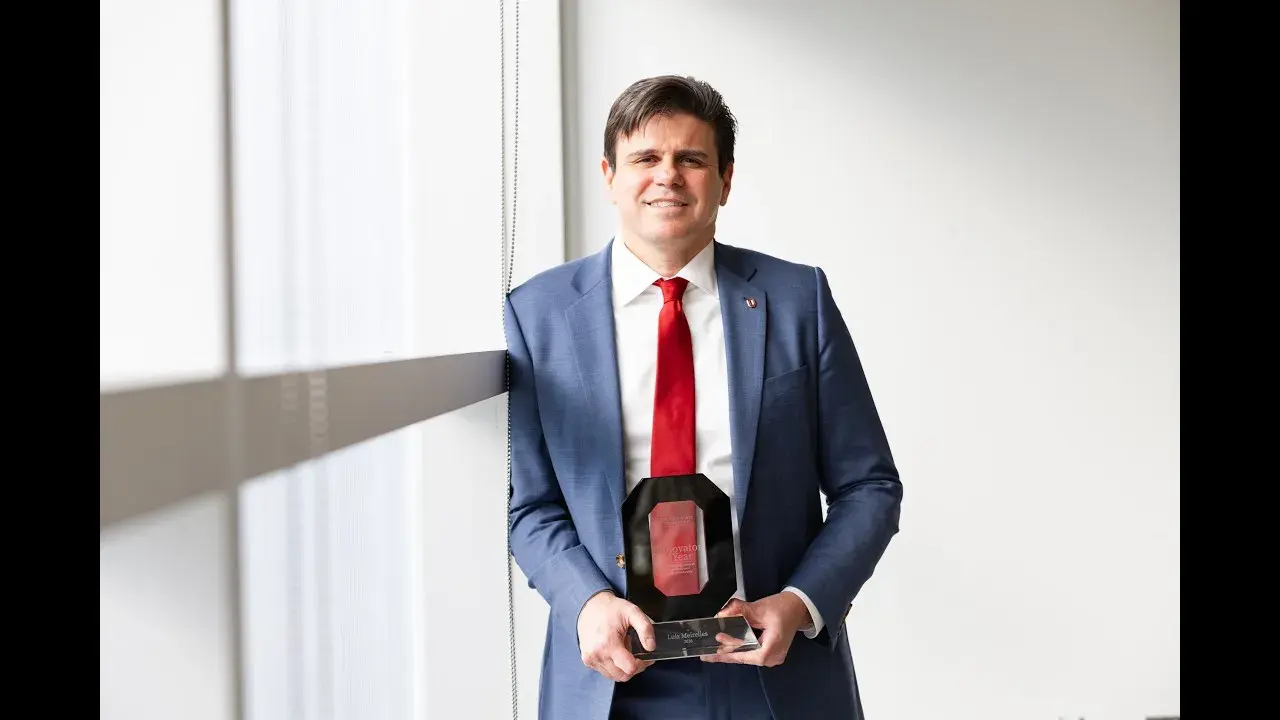 person in a blue blazer and scarlet tie holding an award that resembles a block o