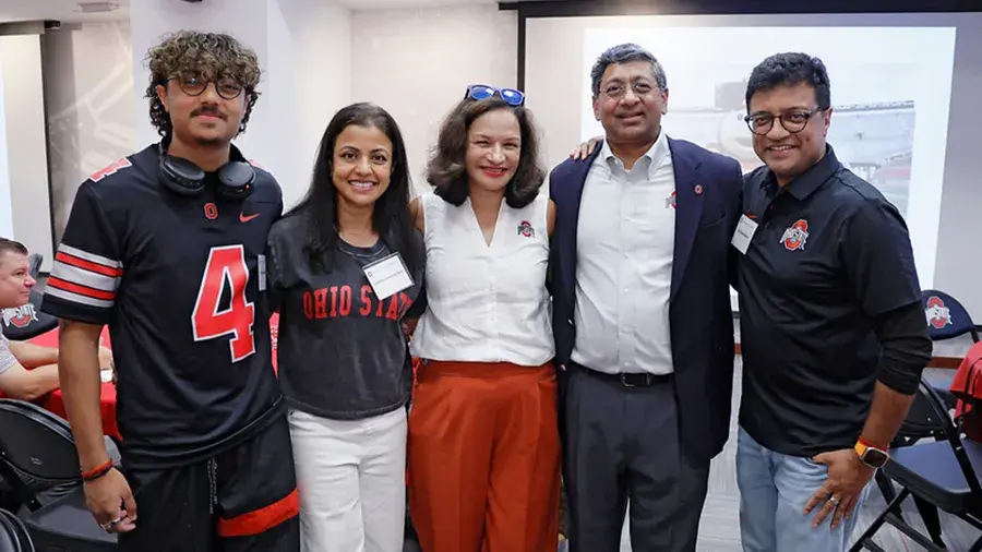 Five people pose together at an indoor Ohio State-themed gathering, standing in front of a projection screen.