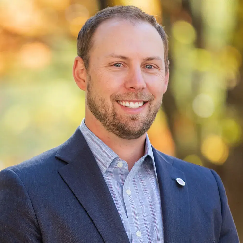 Jake Wozniak smiles and wears a light blue shirt and dark blue suit jacket