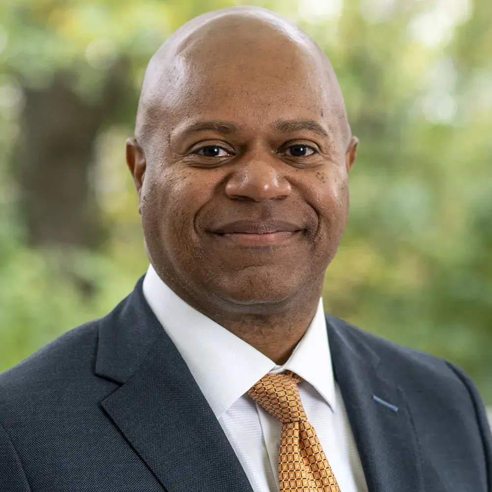 Pierre Bigby stands outside smiling and wearing a gray suit