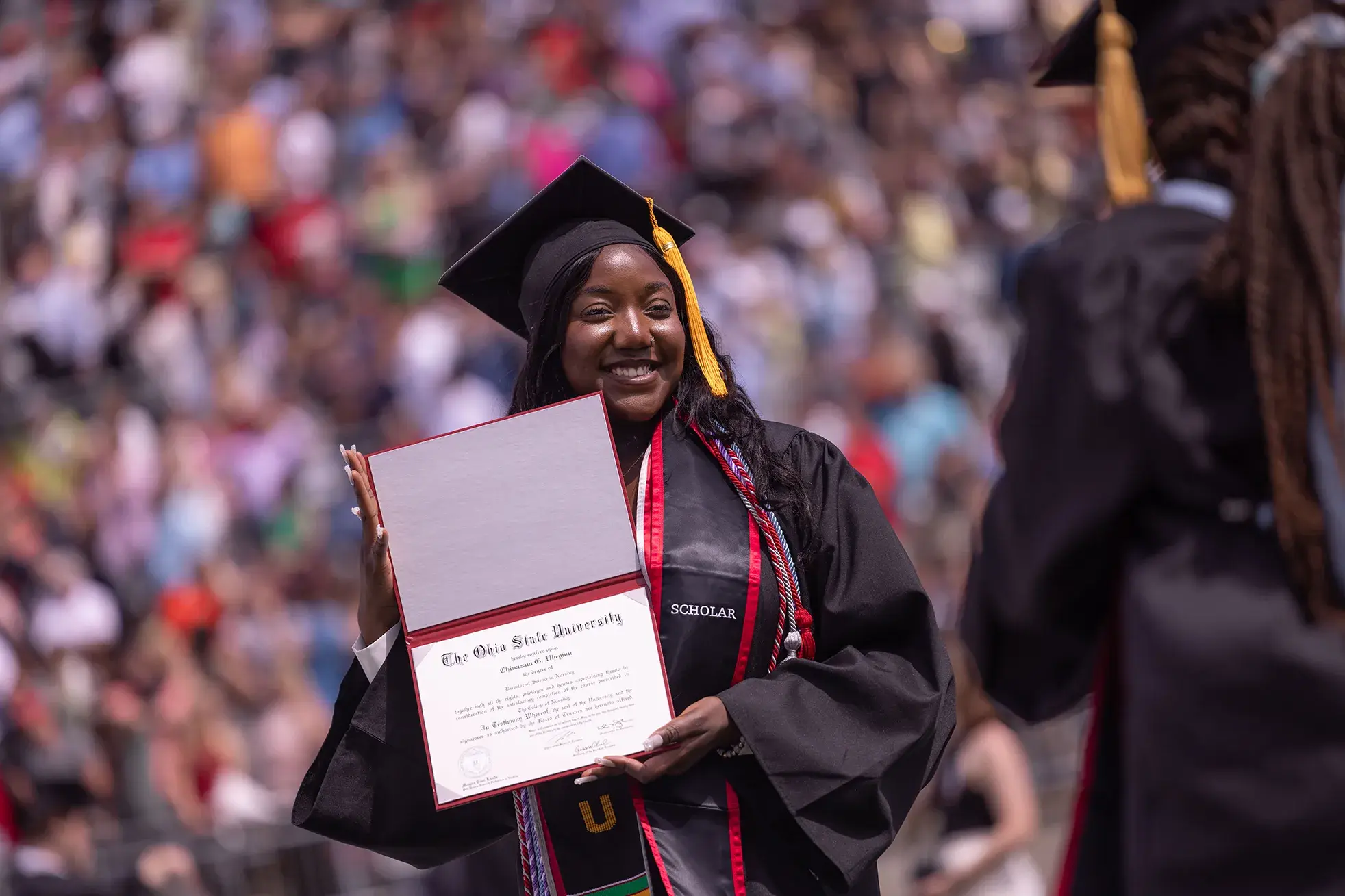student in cap and gown holding her diploma open at graduation ceremony