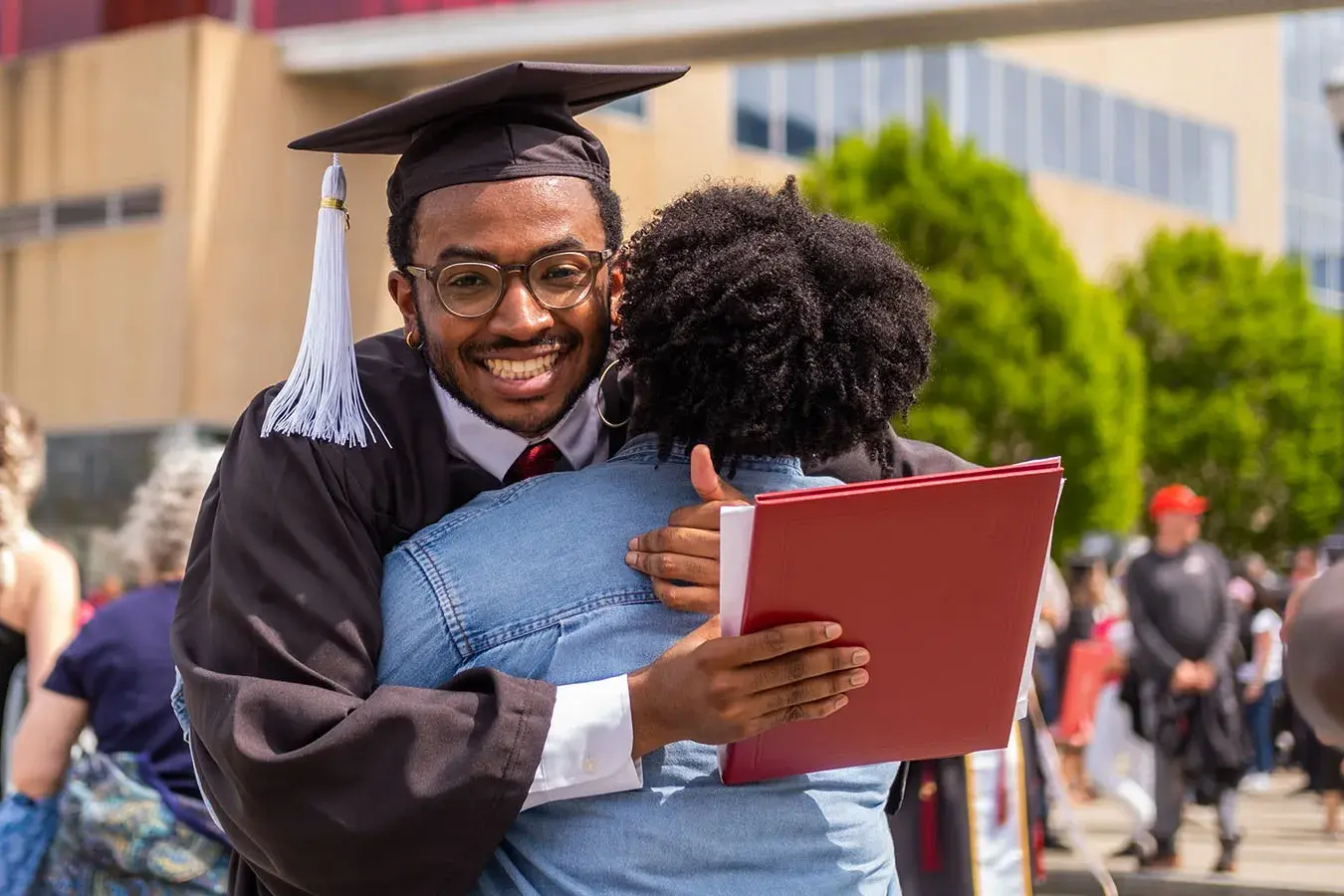 OSU graduate in cap and gown hugs a family member after the ceremony