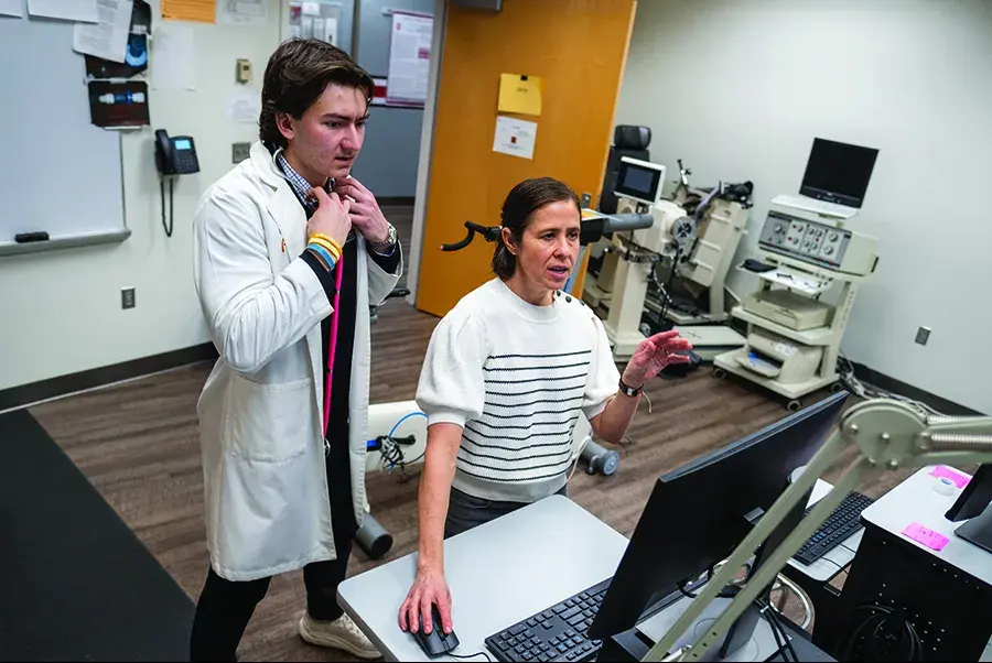 A man wearing a white lab coat and a woman wearing a white and black stripe shirt look at a computer