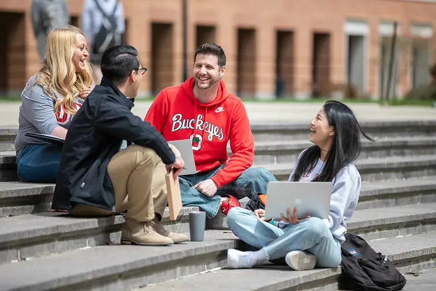 Four people sit outside on steps and talk