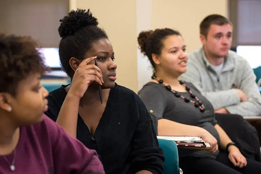 Four students sit in a classroom and appear to be listening to someone speaking