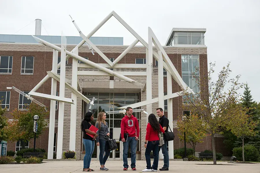 A group of students stand outside of a brick building