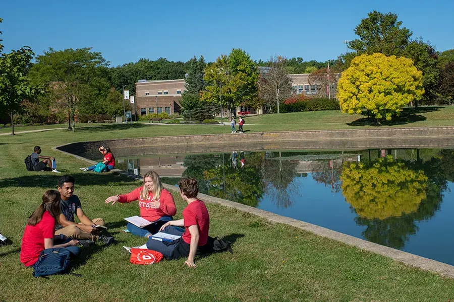 A group of students sit in a circle talking near a small pond