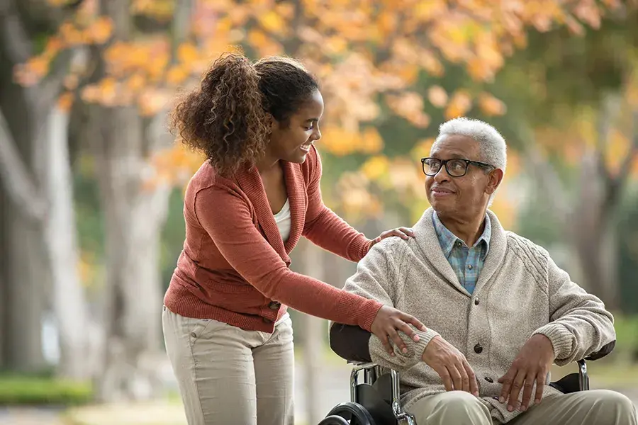 A young woman assists an older man in a wheelchair