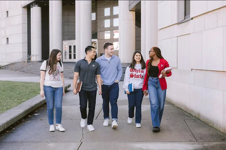 A group of students walk outside in front of a stone building