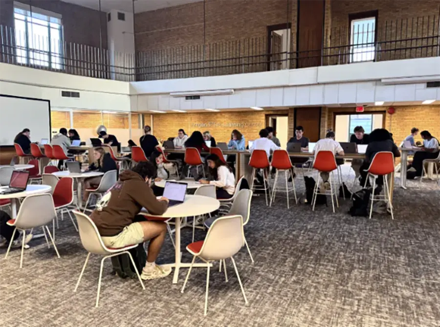 A large group of students sit and study at tables in a large open room