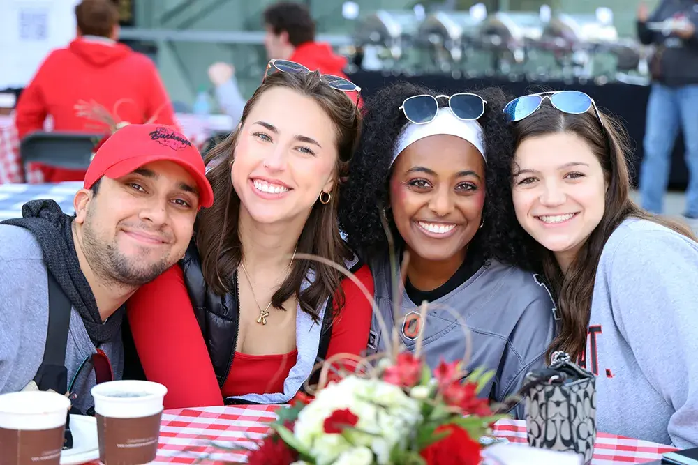 Four students sit outside at a table with a red and white checkered tablecloth and pose for a picture.
