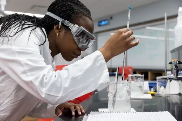 Student working in a lab wearing in a white lab coat and eye protection.
