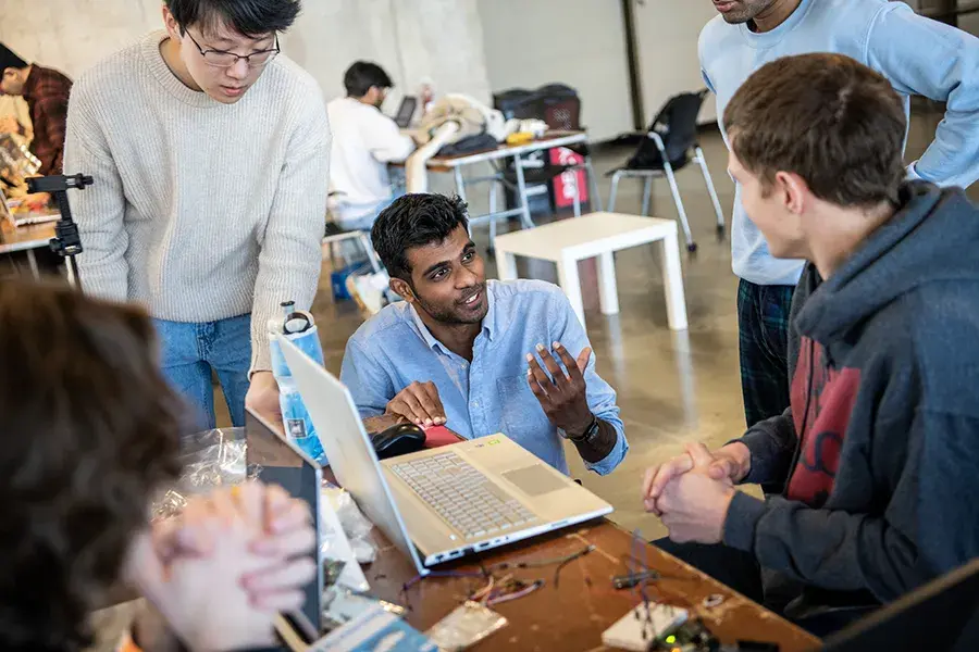 Students in a computer lab having casual conversation around a laptop.