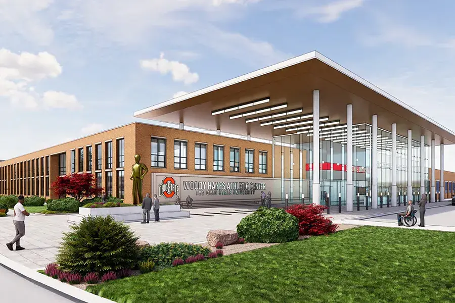 Architectural rendering of the Woody Hayes Athletic Center exterior, featuring a brick-and-glass entrance, large covered canopy, landscaped walkways and several people.