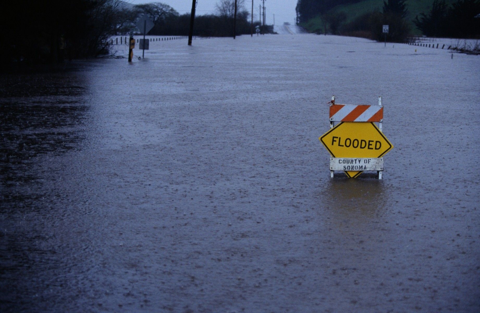 A "flooded" sign sits in the middle of a flooded road.