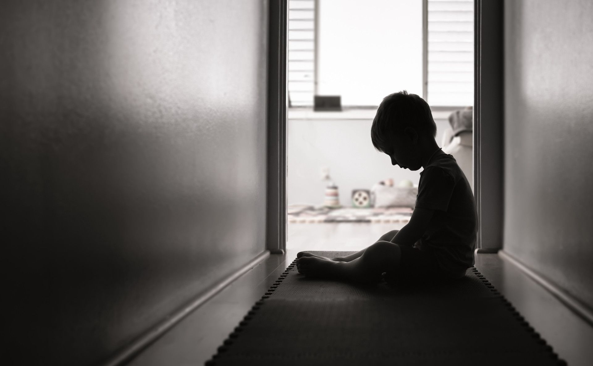 A child sits in shadows at the end of a hallway.