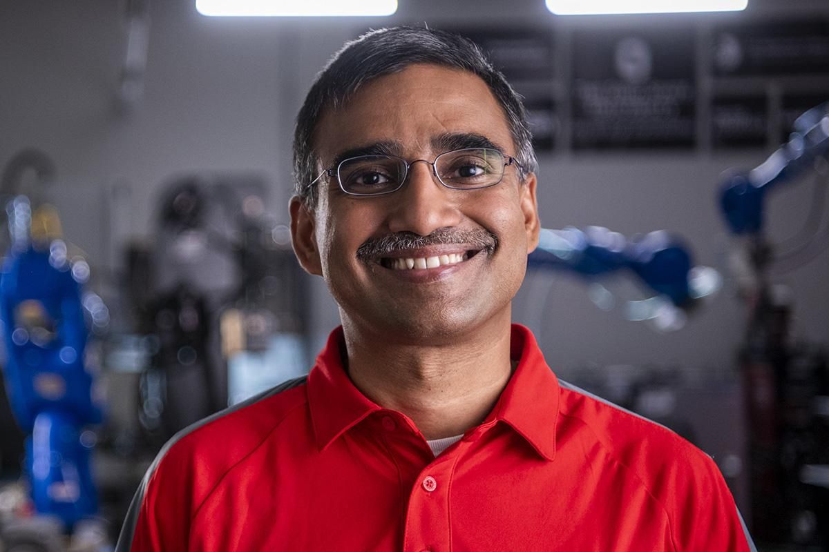 Vimal Buck standing headshot looking into the camera with robotics in the background