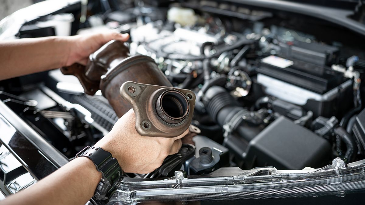 Hands work on a catalytic converter.