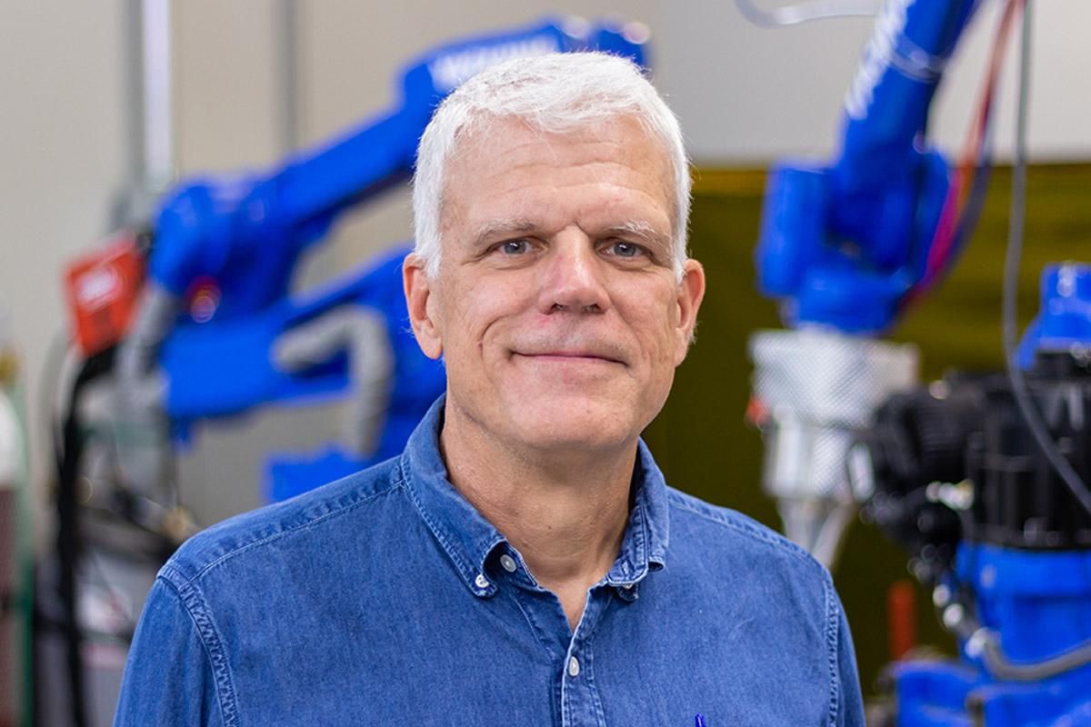 Glenn Daehn headshot looking into the camera with robotics in the background