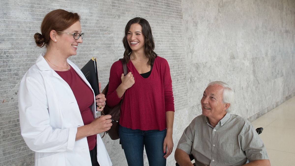 A researcher talks to a man in a wheelchair as a student looks on.