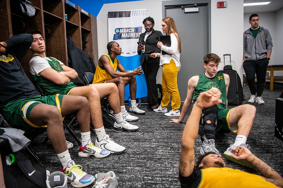 Two Ohio State students talk to a basketball player as they stand in a locker room during the NCAA tournament regional