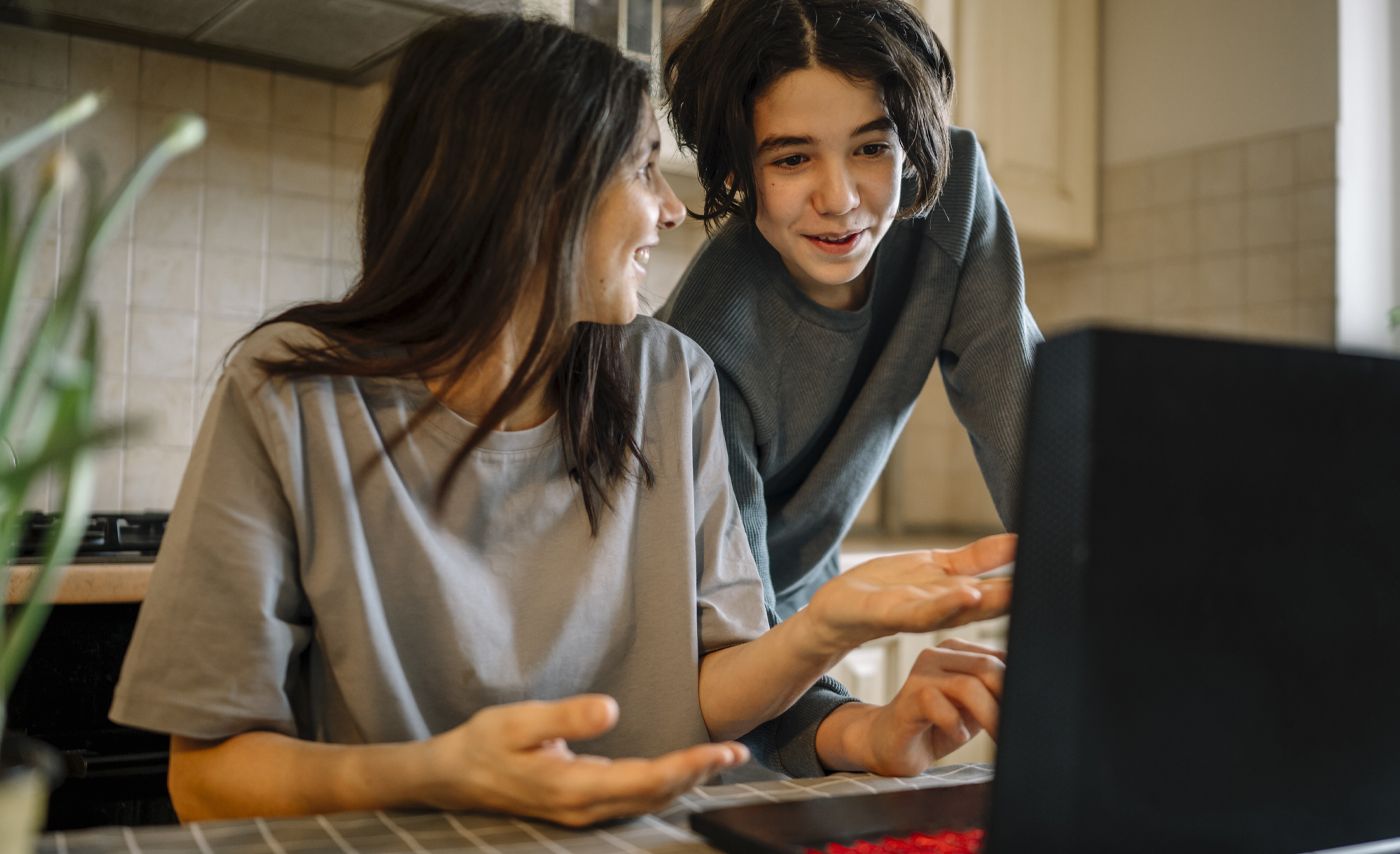 A woman and a boy look at a computer together.