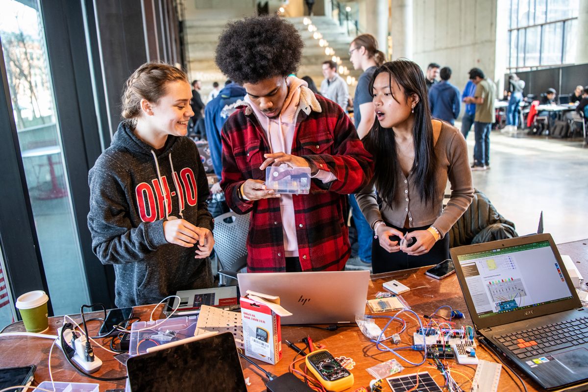 A student works with electronics while two other students look on.