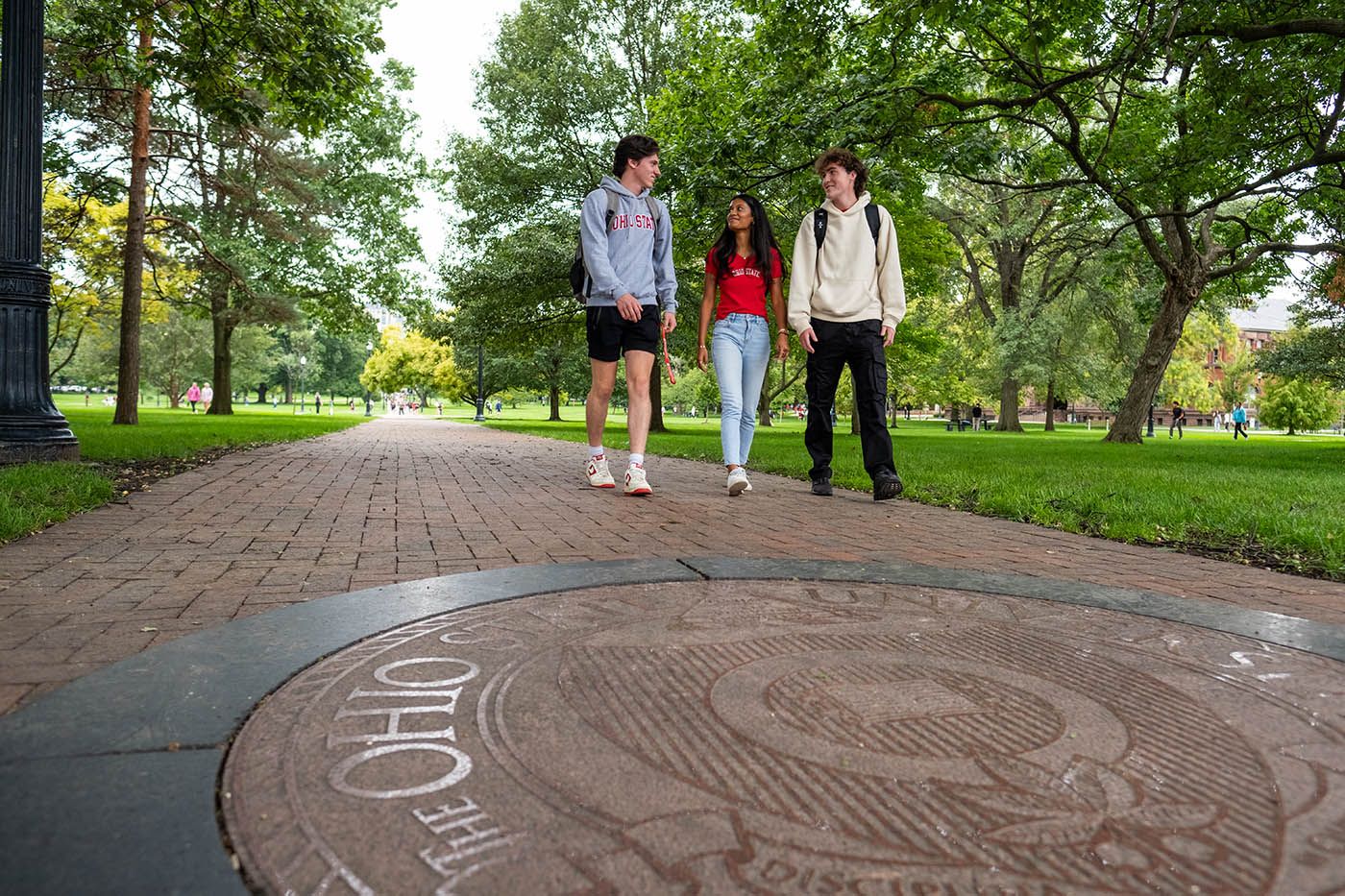 Three Ohio State students walk across the Oval near the university seal.