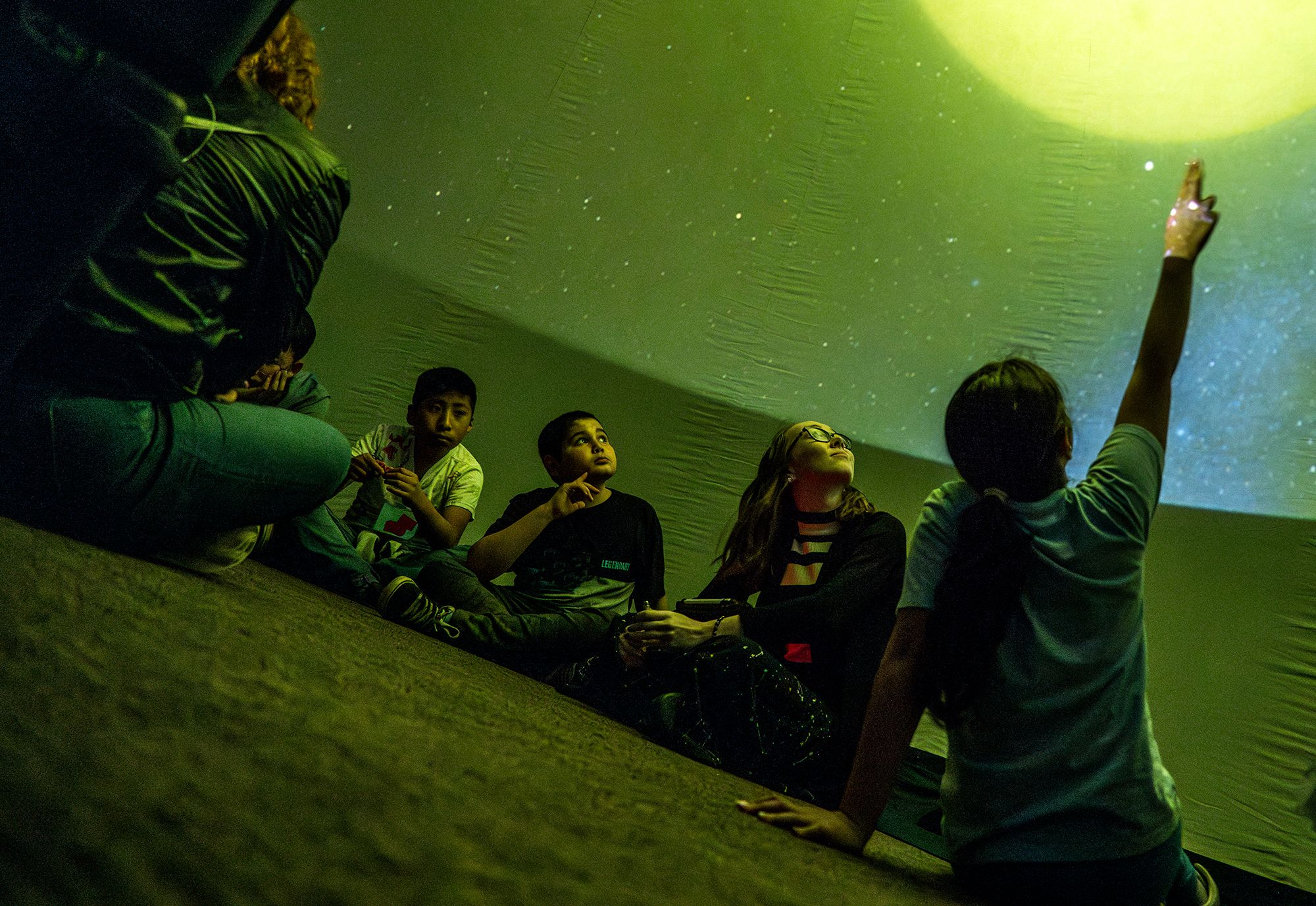 young students sitting on the floor looking up at a planetarium