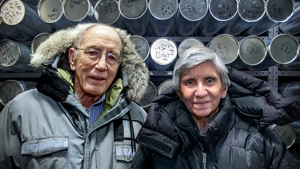 Researcher Lonnie and Ellen Mosley Thompson, clad in winter parkas, stand in front of a wall of ice cores.