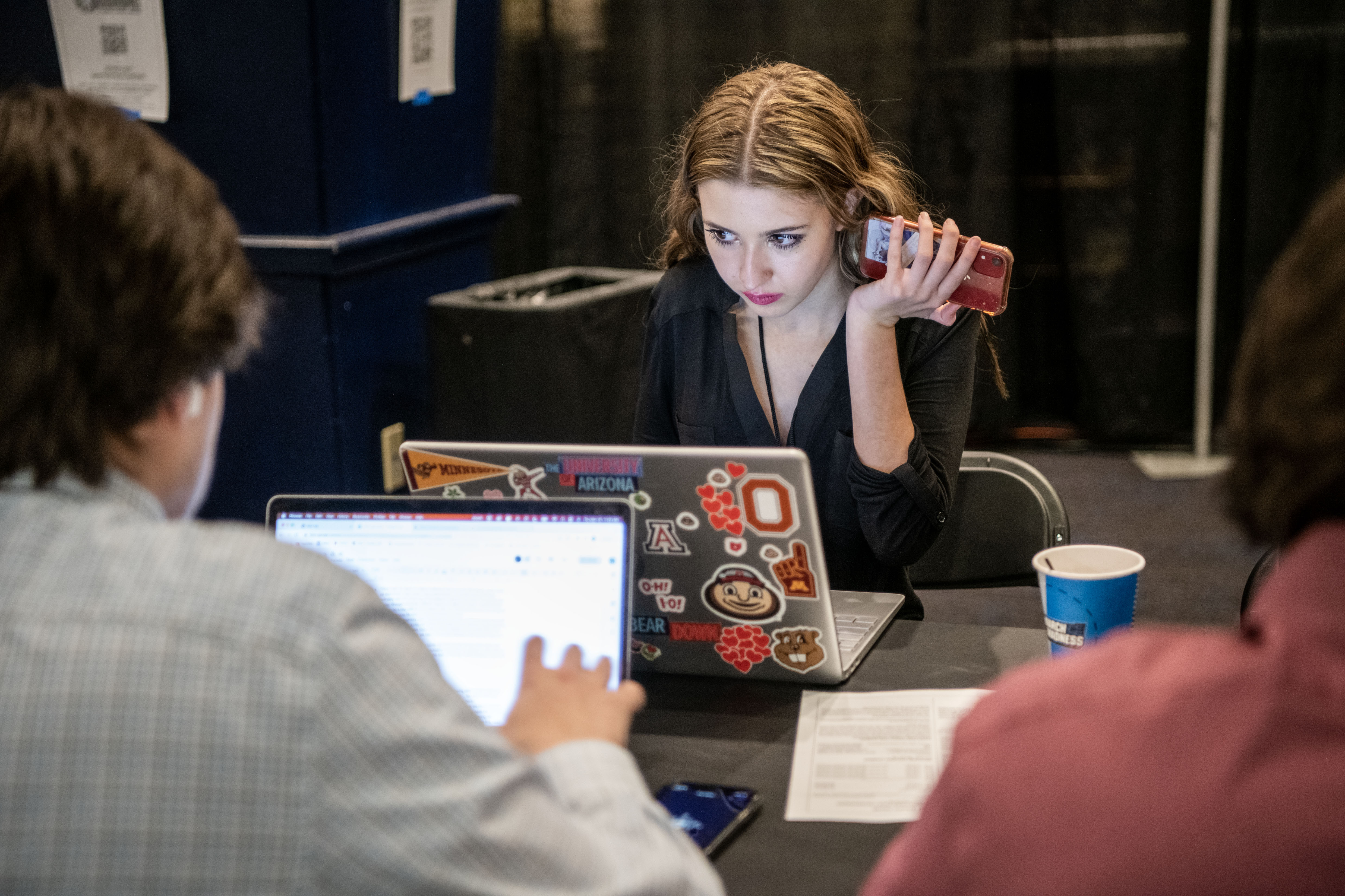 Ohio State student Isabel Mangus transcribes an interview with a phone up to her ear during NCAA mens basketball regional practice sessions.